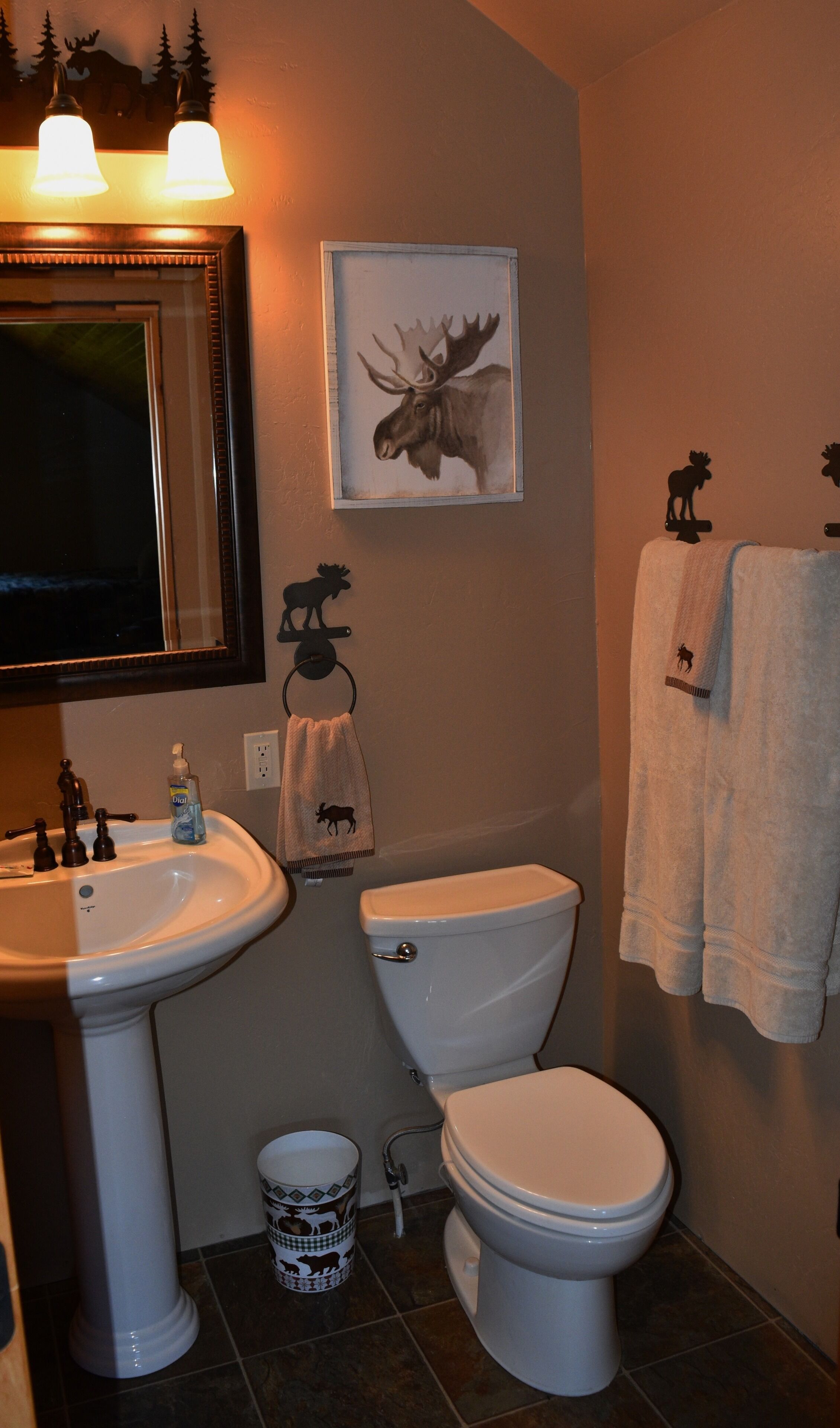 A bathroom with a sink, toilet, and a mirror. There is a framed moose picture on the wall.