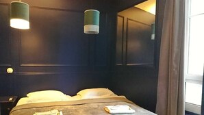 Una habitación de hotel con una cama, dos lámparas colgantes, un espejo grande y una ventana con cortinas.