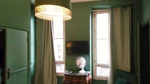 Una habitación con pared verde, un ventanal con cortinas, un escritorio con un globo terráqueo, una silla y un televisor en la pared.