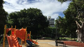 Une aire de jeux avec un toboggan et des structures d’escalade, entourée d’arbres et agrémentée d’un banc.