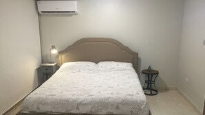 Une chambre à coucher comprenant un lit, une lampe de chevet, une petite table et un appareil de climatisation.