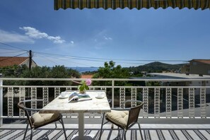 Un balcon avec une table dressée pour deux personnes, offrant une vue panoramique sur un paysage vallonné et un ciel dégagé.