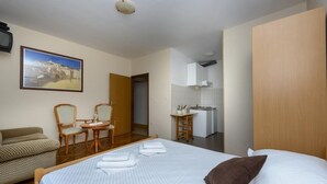 Een hotelkamer met een bed, een bank, een eettafel met stoelen, een keukenhoek en een schilderij aan de muur.