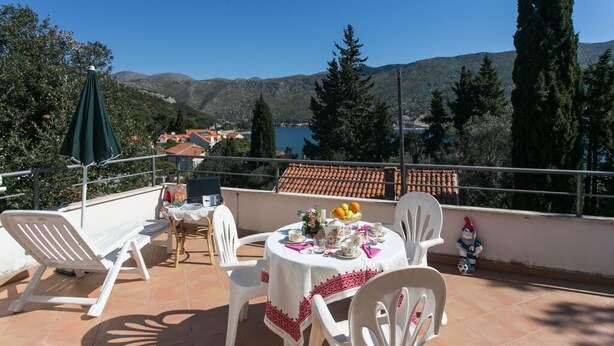 Une terrasse avec une table dressée pour le dîner, offrant une vue panoramique sur un paysage magnifique, avec des montagnes et une étendue d’eau.