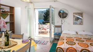 Une chambre à coucher avec un lit, une table sur laquelle se trouvent une bouteille et des verres, une chaise, un miroir et une vue sur l’extérieur.