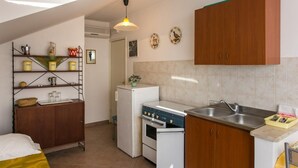 Une cuisine compacte équipée d’une cuisinière, d’un évier et de placards en bois. On y trouve également un petit réfrigérateur et une étagère contenant des ustensiles de cuisine.