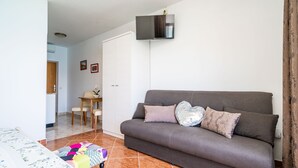 A living room with a sofa, a flat-screen TV mounted on the wall, a dining table with chairs, and a small kitchen area in the background. - Apartments Nikolina (LU) - Studio with Sea View (3 Adults) (Lumbarda)