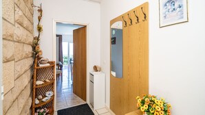 A hallway with a stone wall, a wicker shelf with decorative items, a wooden door with a mirror, and a framed picture on the wall. - Apartments Nikolina (LU) - Studio with Sea View (3 Adults) (Lumbarda)