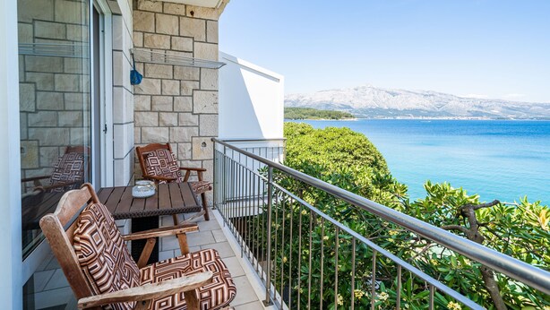 A balcony with a table and chairs, a stone wall, and a view of a body of water and mountains. - Apartments Nikolina (LU) - Studio with Sea View (3 Adults) (Lumbarda)