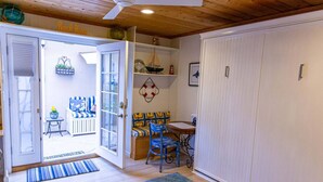 Une pièce avec un plafond en bois, une porte blanche, un banc avec des coussins à rayures, une table avec des chaises et un tapis coloré.