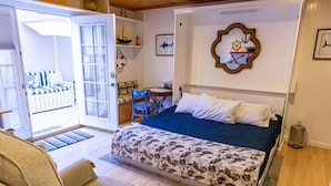 Une chambre à coucher comprenant un lit, une chaise, un bureau et une porte donnant sur un balcon.