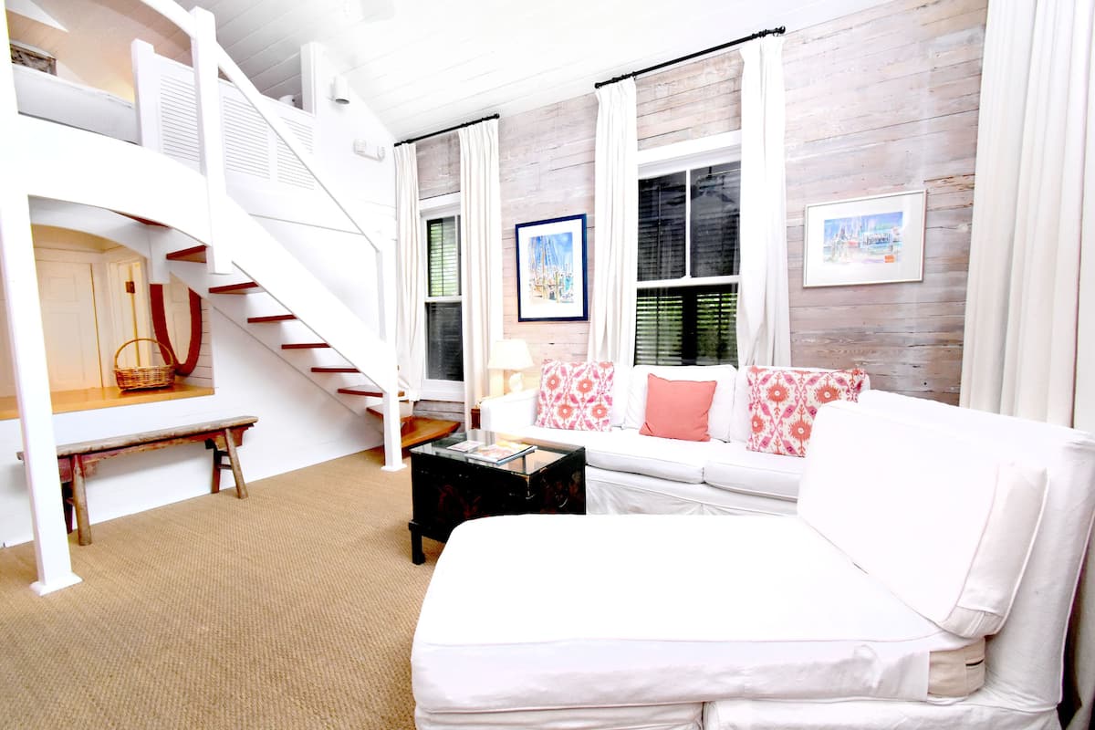 A white staircase leading to an upper level, a white sofa with pink and white pillows, a black coffee table, and a framed picture on the wall.