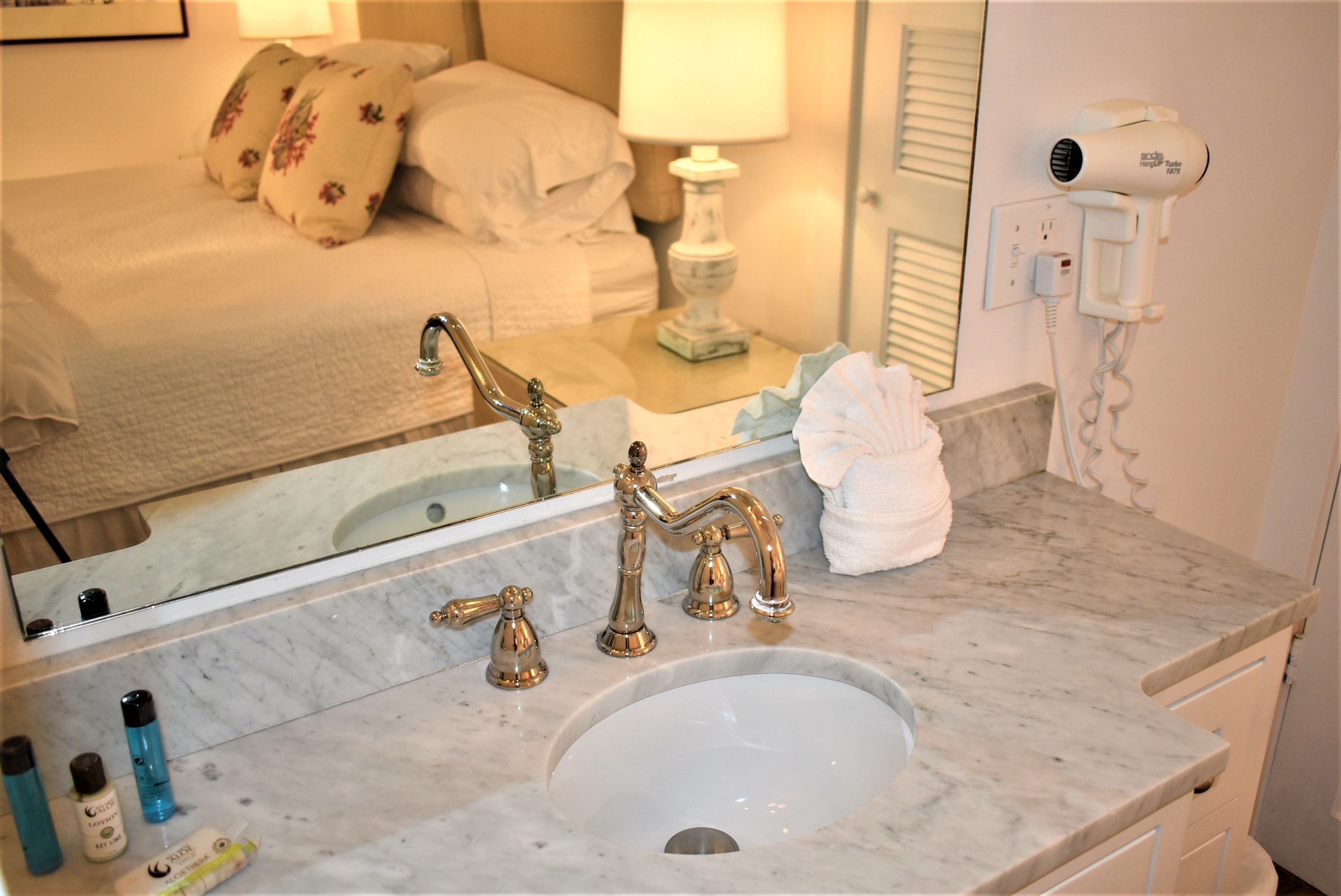 Une salle de bain avec un lavabo en marbre, des robinets dorés et un sèche-cheveux fixé au mur.