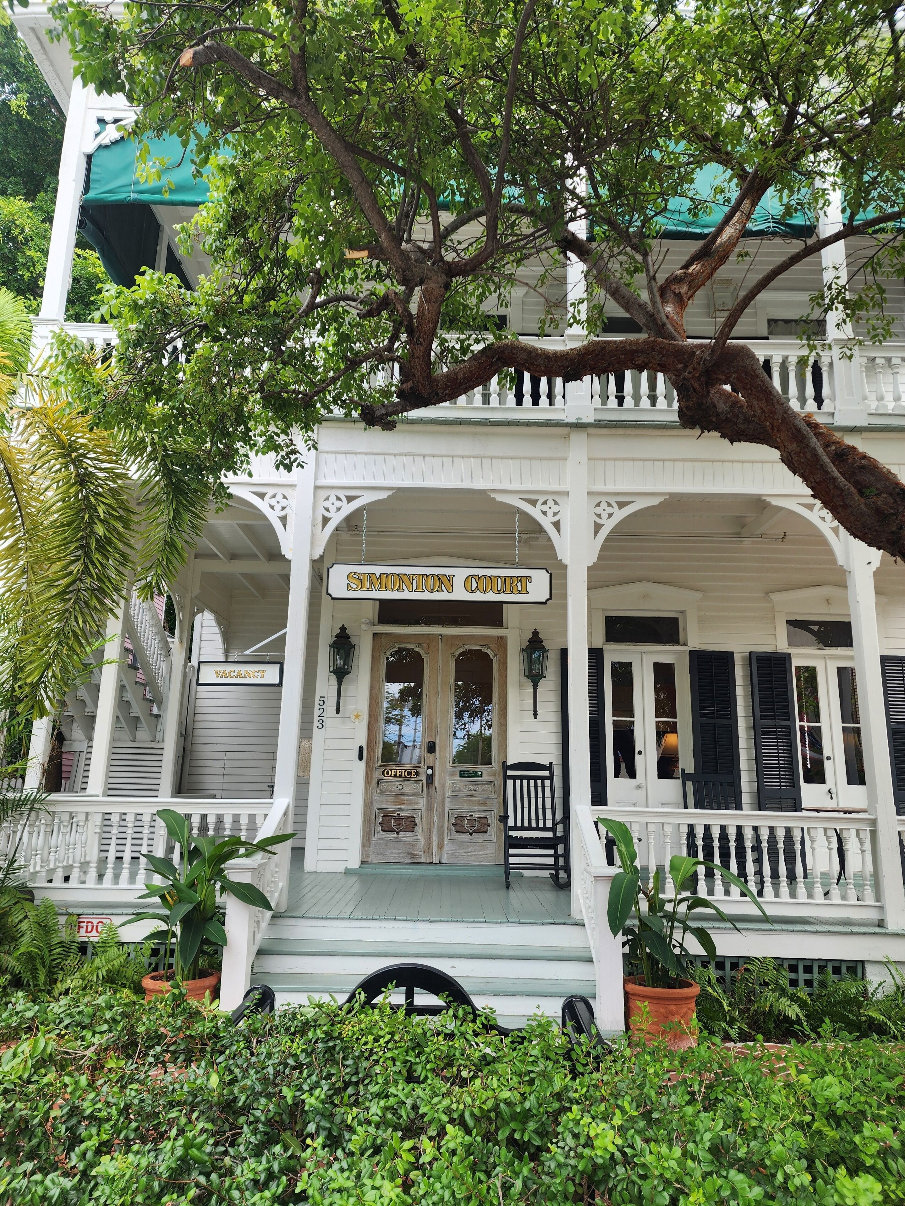 A white building with a porch, a sign reading 'Simonton Court,' and a 'Vacancy' sign.