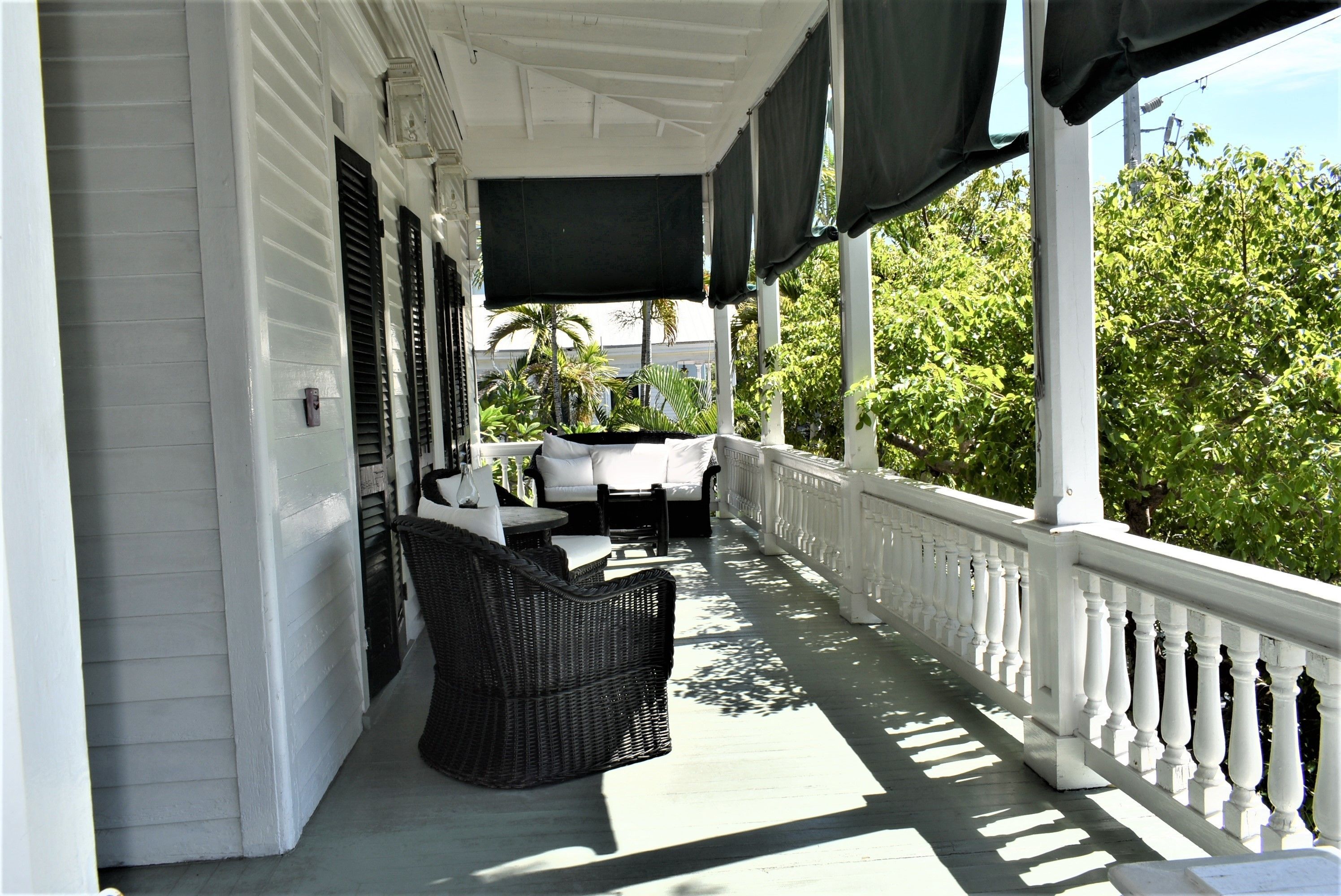 A covered porch with white railings, wicker furniture, and a view of greenery.