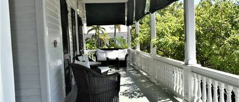A covered porch with white railings, wicker furniture, and a view of greenery.
