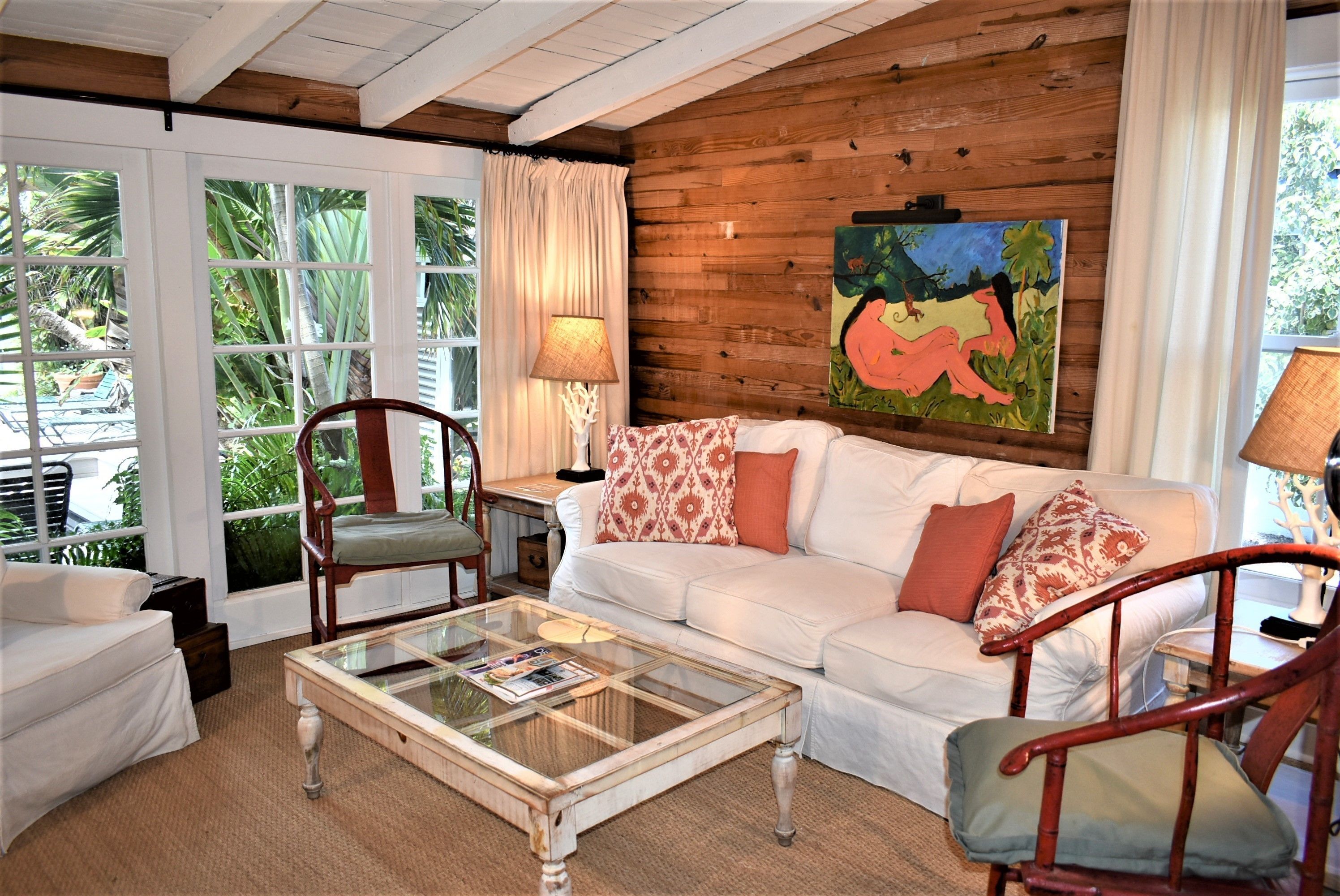 A cozy living room with a white sofa, patterned cushions, a glass coffee table, and wooden walls.