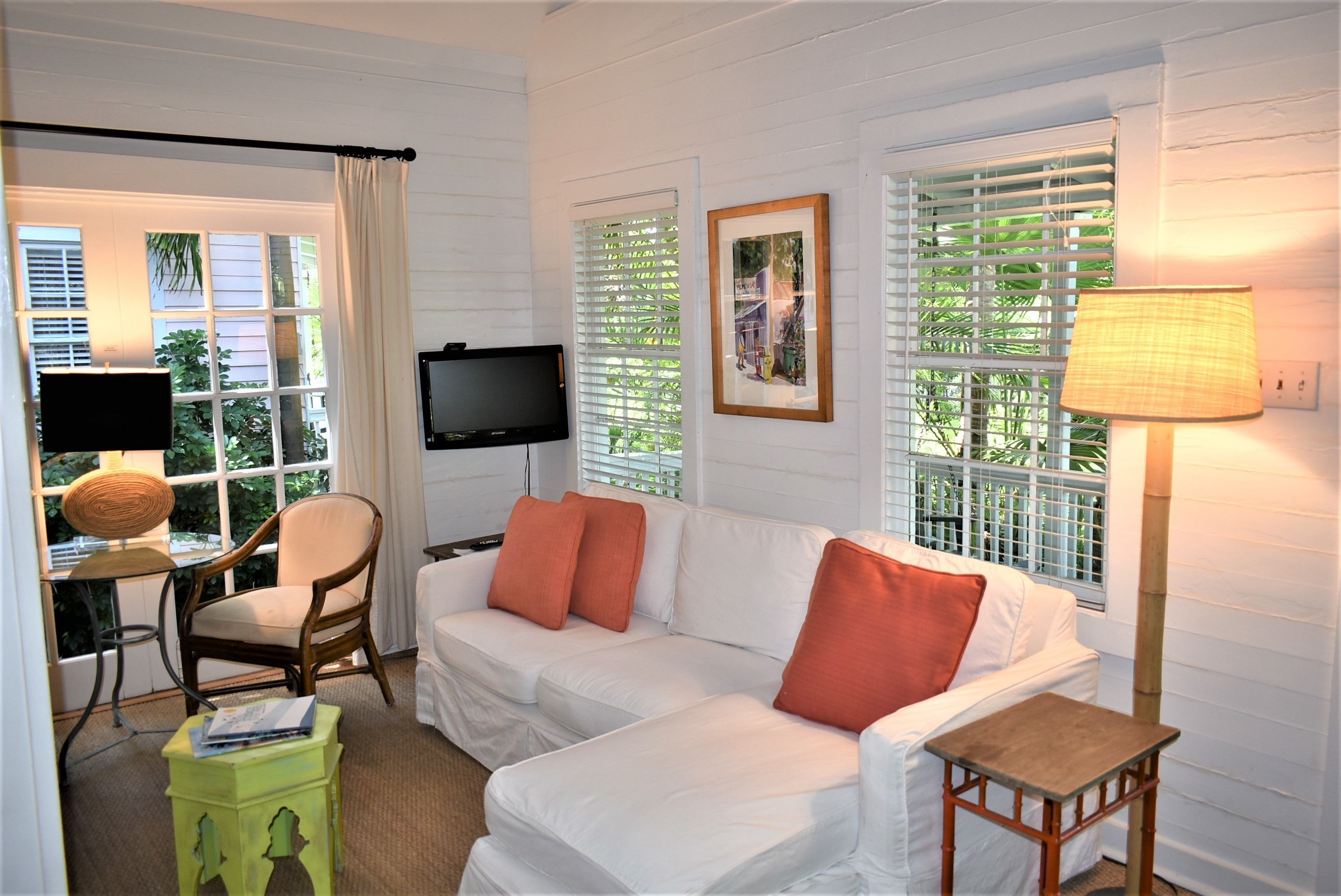 A room with a white sofa, a television, a lamp, and a window with blinds.