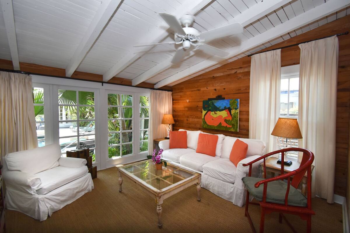 A room with a white sofa, a red chair, a glass coffee table, and a ceiling fan.
