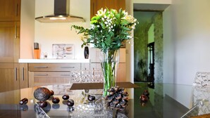 Een moderne keuken met houten kasten, een roestvrijstalen afzuigkap en een glazen tafel met een vaas bloemen en dennenappels.