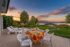 Un espace de restauration en plein air avec une table dressée pour six personnes, entourée de chaises blanches, sous un ciel au coucher du soleil.