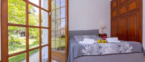 A bedroom with a large window, a bed with a floral bedspread, and wooden furniture.