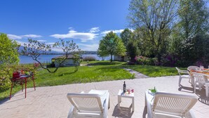 An outdoor patio with white lounge chairs and a table, overlooking a grassy area and a body of water.