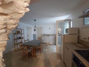 A dining area with a table and chairs, a kitchen with cabinets and appliances, and a stone wall. - Charming cottage of 60m2 (Châteauneuf-Val-Saint-Donat)
