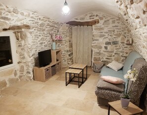 A cozy stone-walled room with a television, a wooden table, a sofa, and a potted plant. - Charming cottage of 60m2 (Châteauneuf-Val-Saint-Donat)