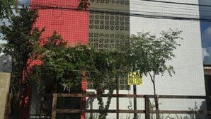 Un edifici amb façana vermella i blanca, una entrada tancada per una reixa i un petit arbre al primer pla.