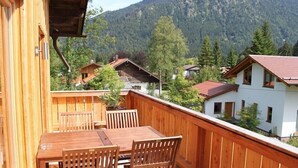 Une terrasse en bois avec une table et des chaises, donnant sur une région montagneuse parsemée de maisons.