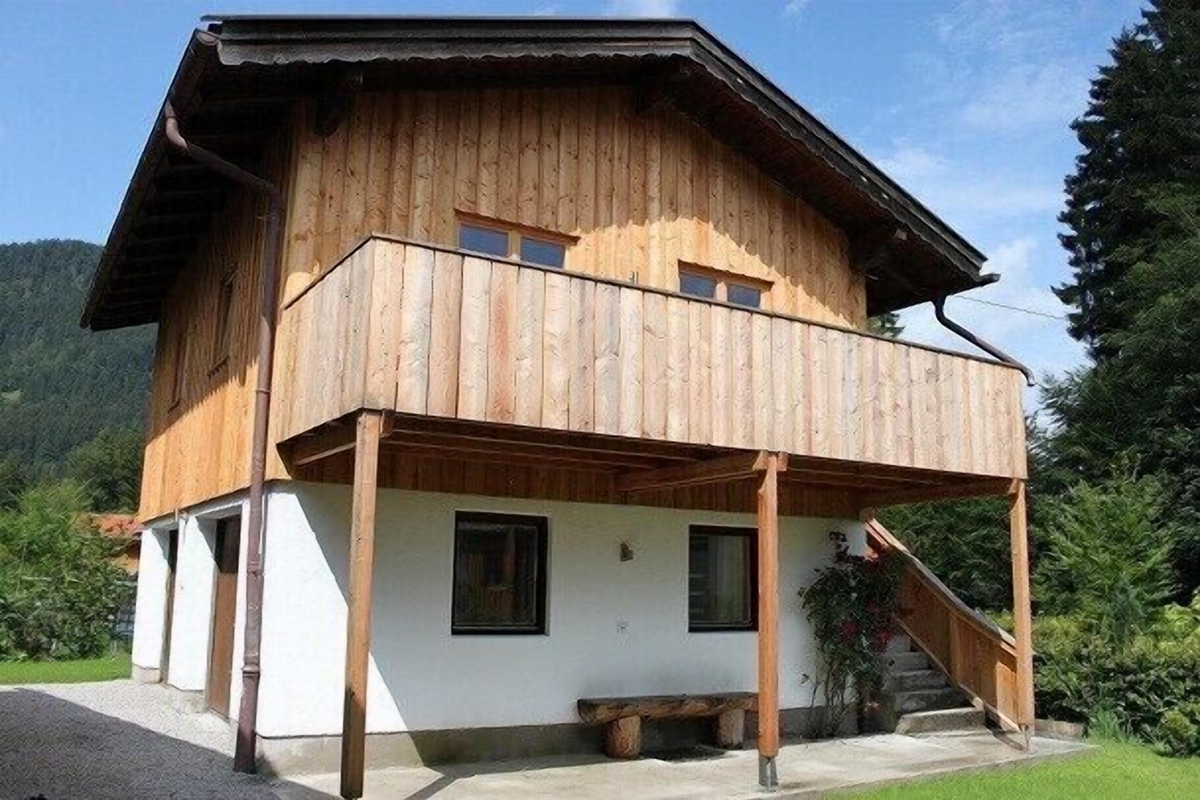 A wooden chalet with a balcony, a staircase, and a white exterior wall.