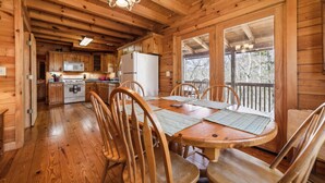 Una baita in legno con zona pranzo, cucina e un balcone affacciato sugli alberi.