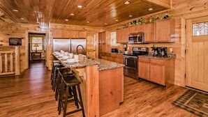 Una cocina estilo cabaña de madera con una isla central, taburetes de bar, electrodomésticos de acero inoxidable y techo de madera.