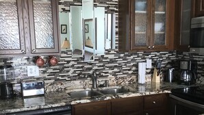 A kitchen with granite countertops, stainless steel appliances, and dark wooden cabinets. - Direct Ocean View from the top floor! (Orange Beach)