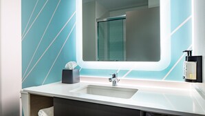 Un baño con un lavamanos blanco, un espejo y un perchero para toallas.
