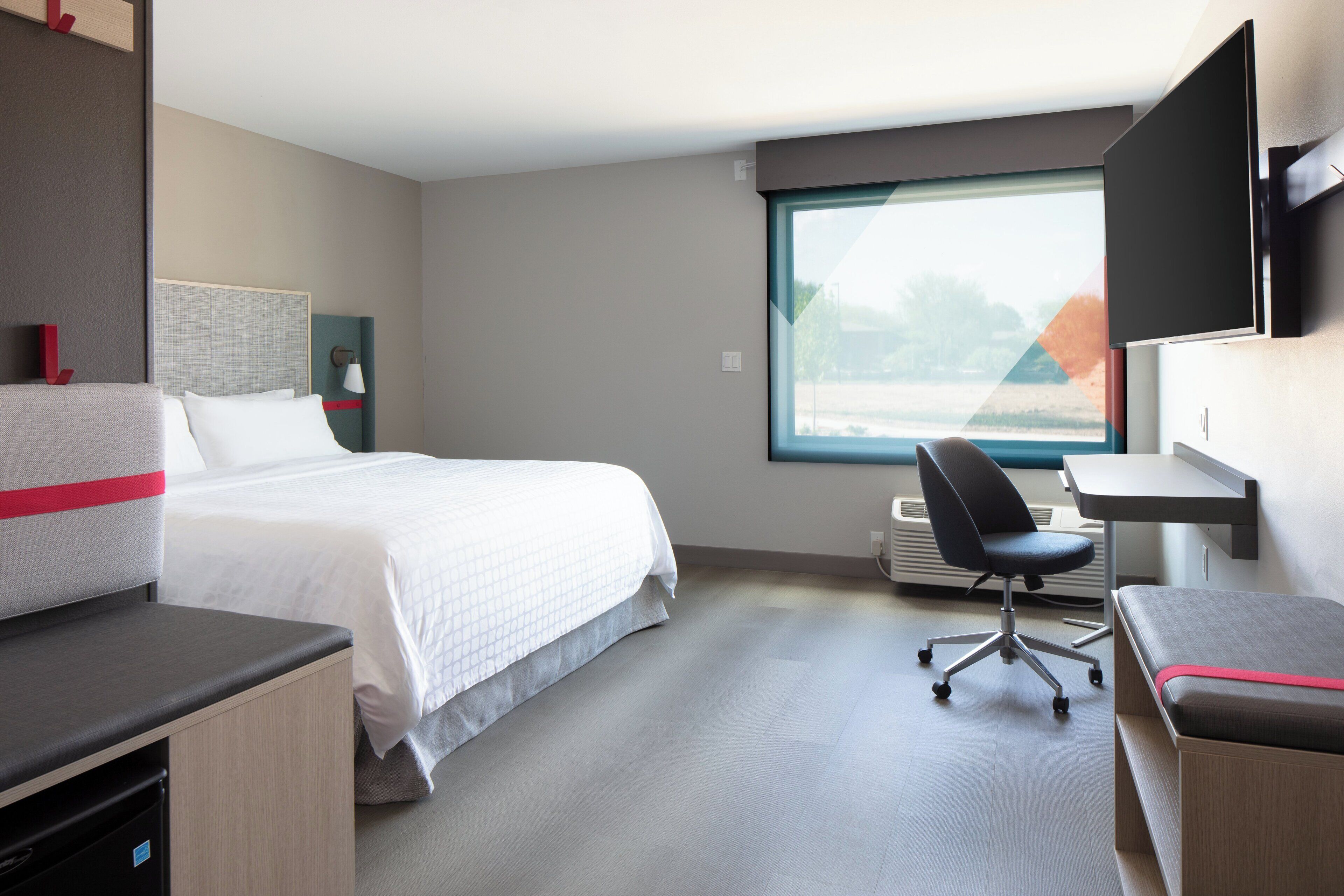 A hotel room with a bed, a desk, a chair, and a large window.