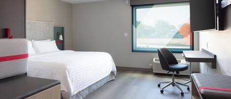 A hotel room with a bed, a desk, a chair, and a large window.