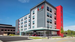 A modern hotel building with a prominent 'avid' sign, a red accent wall, and a covered entrance area. - avid hotels Madison - Monona by IHG (Madison)