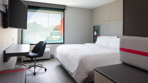 Una habitación de hotel con una cama, un escritorio, una silla y un televisor montado en la pared.