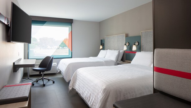 Una habitación de hotel con dos camas, un escritorio, una silla y un televisor.