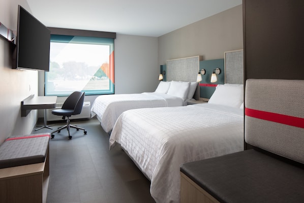Una habitación de hotel con dos camas, un escritorio, una silla y un televisor.