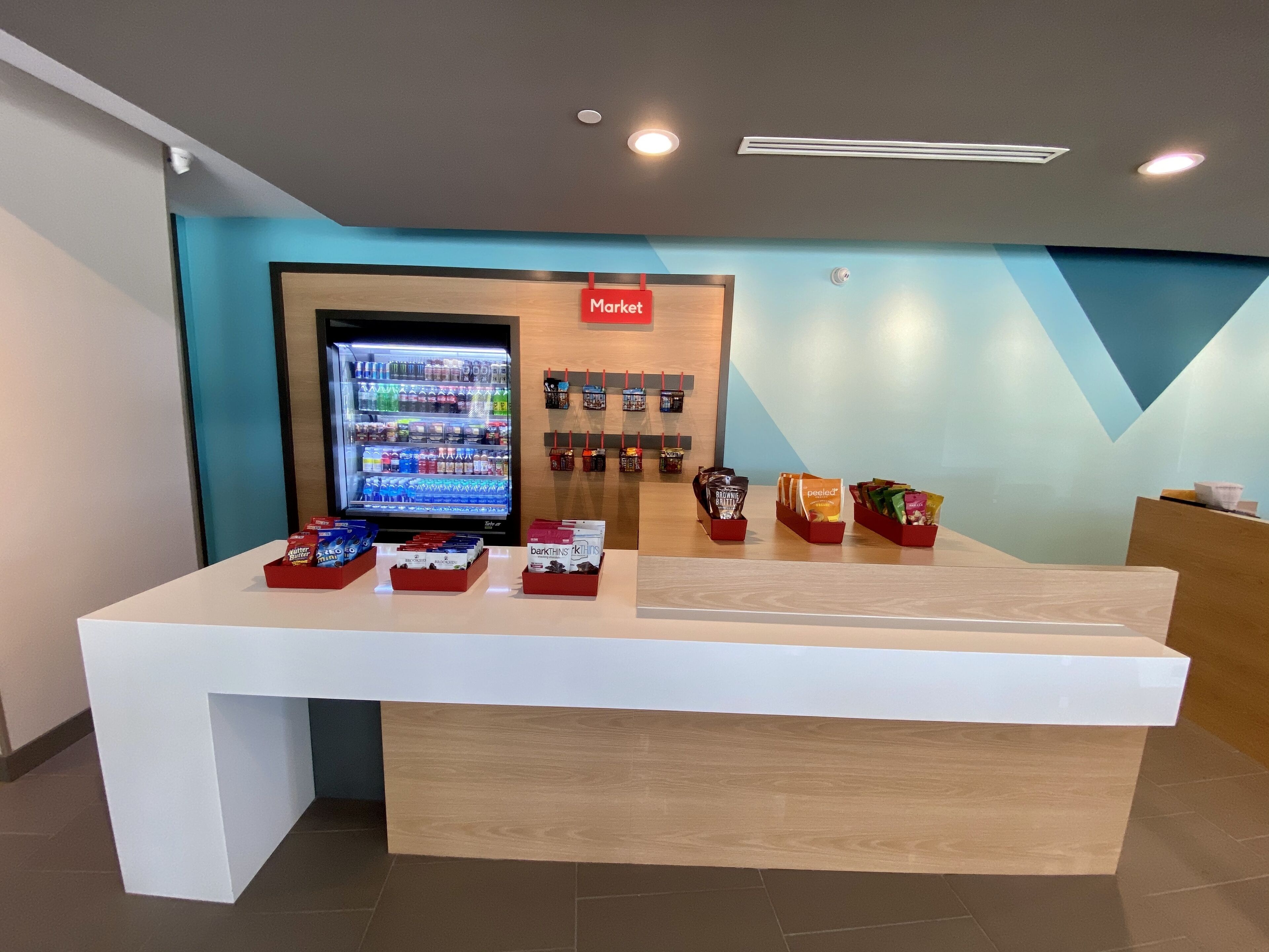 Zona de recepción con máquina expendedora, exhibición de snacks y un letrero que dice 'Market'.