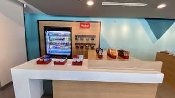 Zona de recepción con máquina expendedora, exhibición de snacks y un letrero que dice 'Market'.