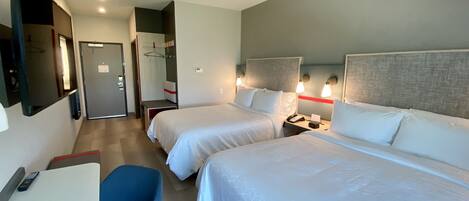 Quarto de hotel com duas camas, uma escrivaninha, uma cadeira e um guarda-roupa.
