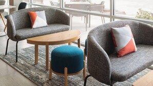 A modern interior with grey upholstered chairs, a wooden table, and a large window offering a view of the outdoors. - avid hotels Beaumont by IHG (Beaumont)