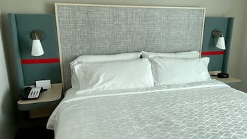 Habitación de hotel con una cama grande, dos mesitas de noche, un teléfono y un reloj digital.