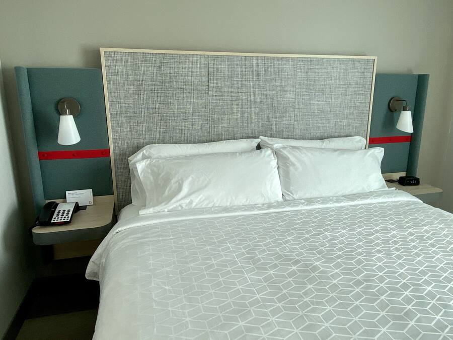 Habitación de hotel con una cama grande, dos mesitas de noche, un teléfono y un reloj digital.