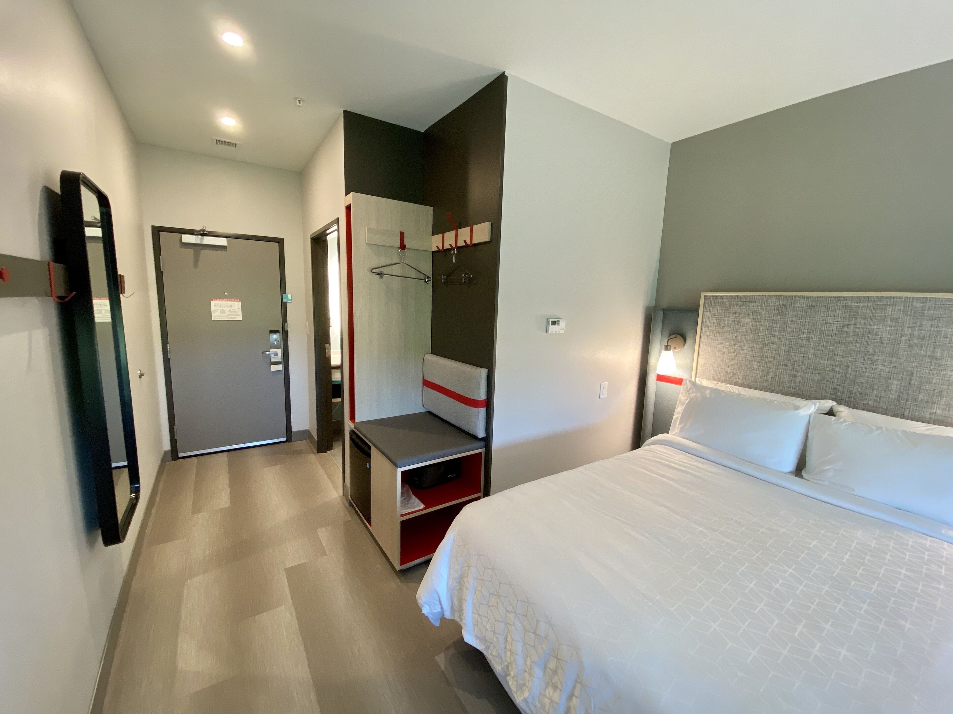 Une chambre d’hôtel avec un lit, un bureau, une armoire et un miroir.