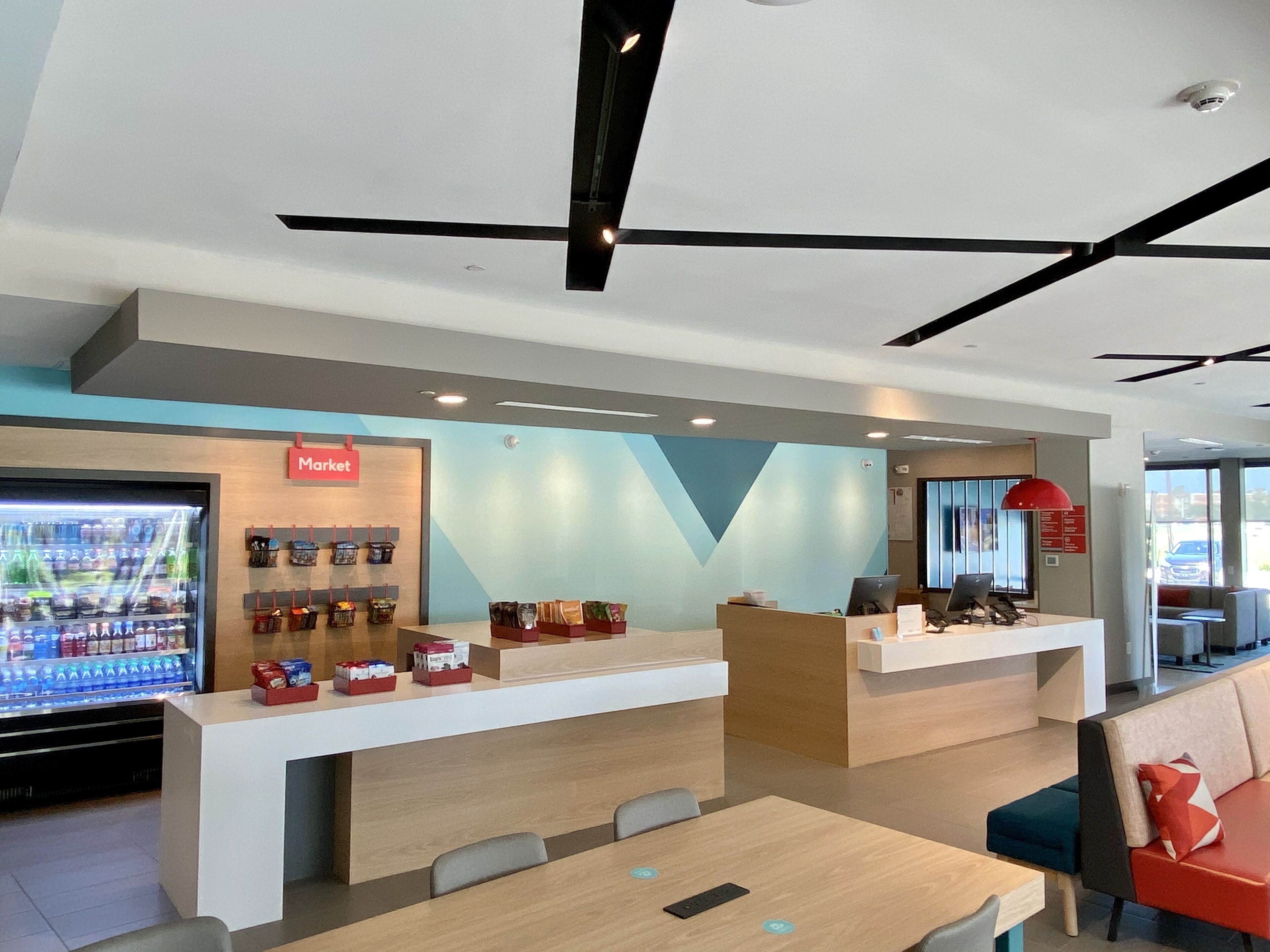 A modern hotel lobby with a reception desk, a market area, and seating arrangements.